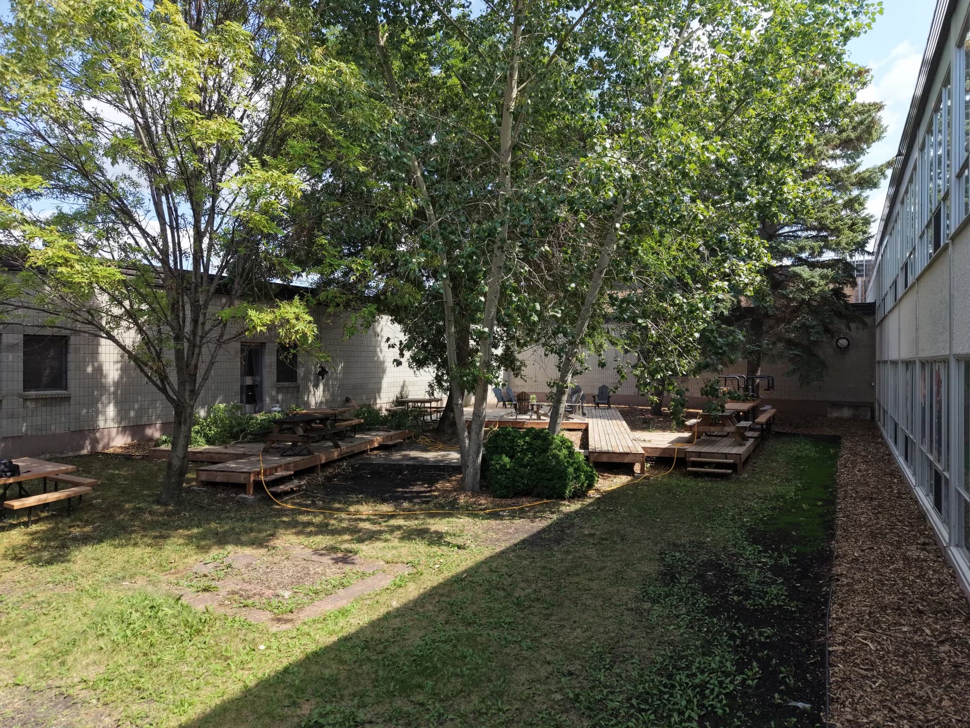 Westwood Collegiate courtyard with mature trees, wooden seating areas and landscaped beds beside the school